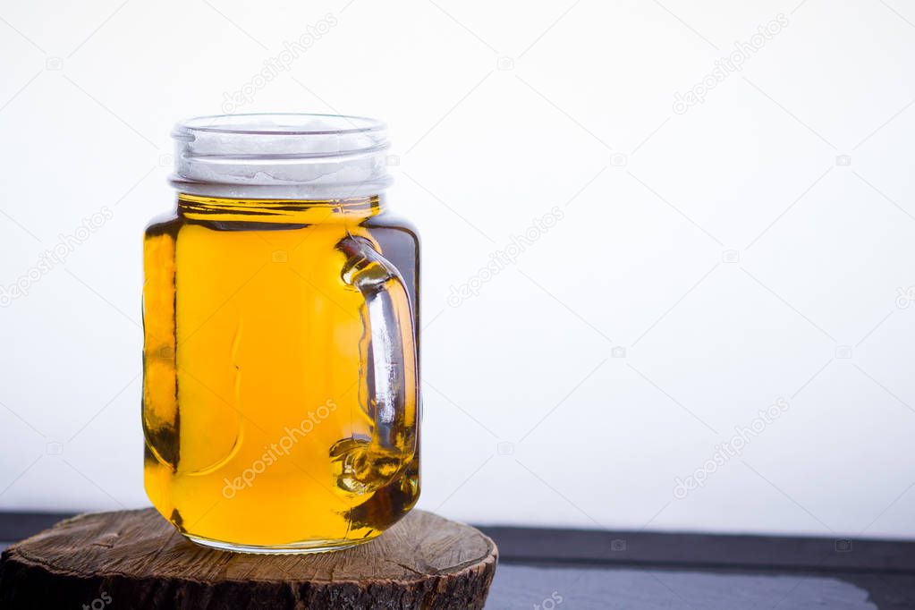 Beer with foam in mason jar on a white background. A glass of light beer on a wooden stand. Low alcohol drink on slate board. Copy space