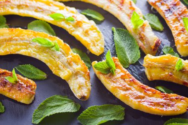 Siyah mutfak tahtası ve şist taşı üzerinde ızgara muz yarım. Siyah arka planda nane ile Fırında muz tatlısı. Asya sağlıklı gıda. Görünümü kapat