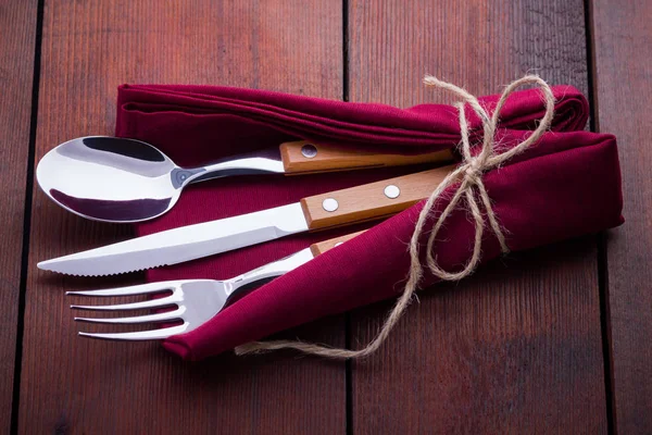 Rustic set of cutlery knife, spoon, fork. utlery with burgundy napkin and twine. Wooden background. Copy space. Top view