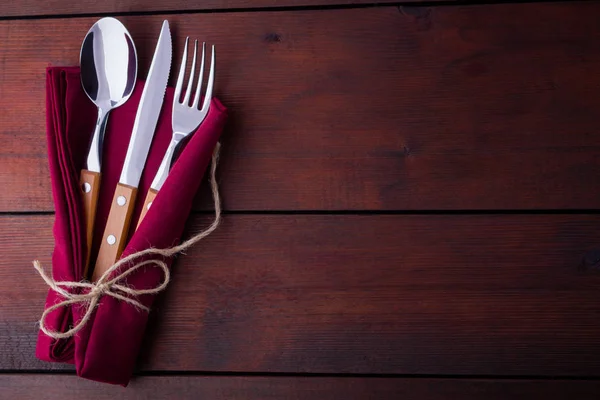Rustic set of cutlery knife, spoon, fork. utlery with burgundy napkin and twine. Wooden background. Copy space. Top view