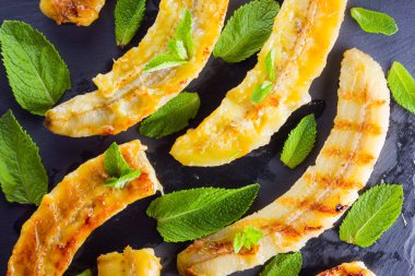 Siyah mutfak tahtası ve şist taşı üzerinde ızgara muz yarım. Siyah arka planda nane ile fırında muz tatlısı. Asya sağlıklı gıda