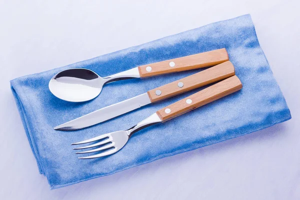 Cutlery set. Knife, fork, spoon on blue napkin. Table setting. Cutlery with wooden handles on a white background. Top view