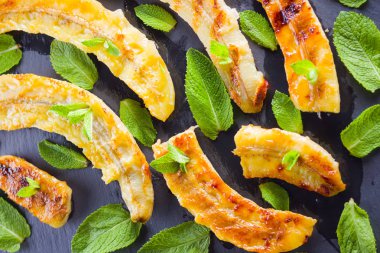 Siyah mutfak tahtası ve şist taşı üzerinde ızgara muz yarım. Siyah arka planda nane ile fırında muz tatlısı. Asya sağlıklı gıda