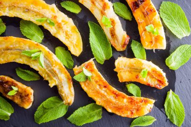 Siyah mutfak tahtası ve şist taşı üzerinde ızgara muz yarım. Siyah arka planda nane ile fırında muz tatlısı. Asya sağlıklı gıda