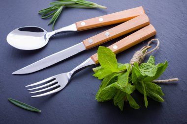 Çatal bıçak takımı. Bıçak, kaşık, tahta taş üzerinde çatal. biberiye ve nane ile utlery. Siyah arka plan. Kopya alanı. Üstte görüntü