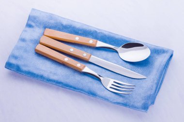 Çatal bıçak takımı. Bıçak, çatal, mavi peçete üzerine kaşık. Masa ayarı. Beyaz arka plan üzerinde ahşap saplı çatal bıçak takımı. Üstte görüntü