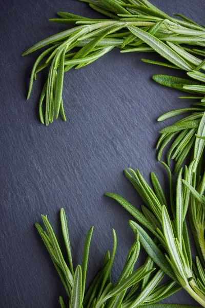 Rosemary branches on black background. Fresh rosemary on slate stone. Herbs for cooking meat dishes with copy space. Top view