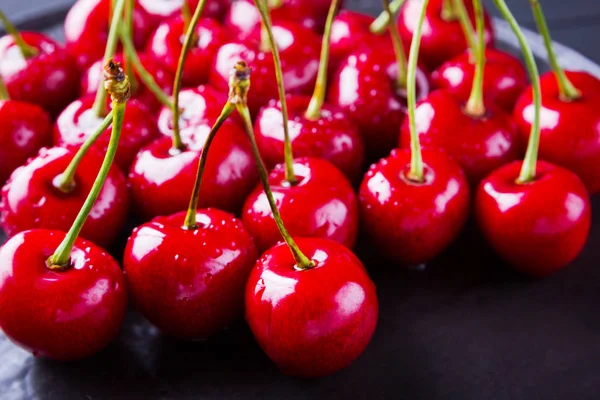 Red cherries on a black background. Sweet cherries in water drops on a dark background. Red berries for vegan. Top view