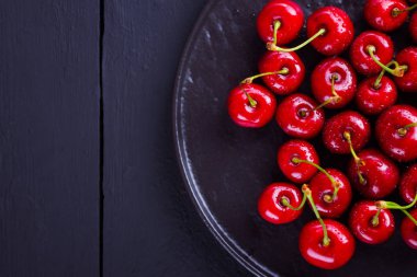 Siyah tabakta kırmızı kirazlar. Karanlık bir arka plan üzerinde su damlatatlı kiraz. Vegan için kırmızı meyveler. Üst te. Kopyalama alanı