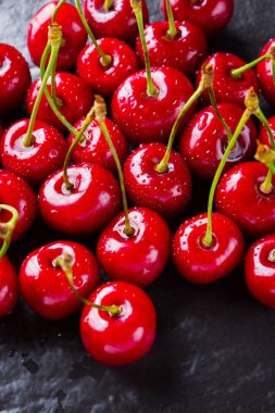 Siyah bir arka plan üzerinde kırmızı kiraz. Karanlık bir arka plan üzerinde su damlatatlı kiraz. Vegan için kırmızı meyveler. Üstte görüntü