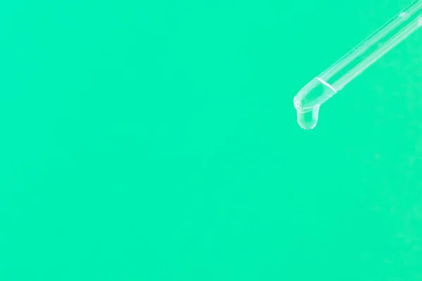 Serum for cosmetic procedures. Serum on a green background. Cosmetic pipette with a drop. Minimalism. Close up