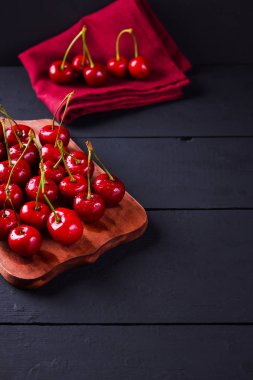 Karanlık bir arka planda kiraz. Tahta tahtada kırmızı kirazlar. Kırmızı bir peçete üzerinde su damlaları çilek. Sağlıklı yiyecekler. Kopyalama alanı