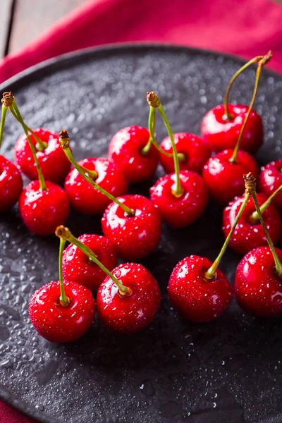 Cherries on a black plate. Sweet cherries on a wooden board. Red berries in drops of water on a red napkin. Rustic style. Copy space