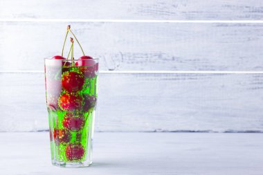 Vişne kokteyli. Beyaz arka plan üzerinde bir bardak kırmızı kiraz. Tatlı kiraz ile yeşil gazlı içecek. Kopyalama alanı