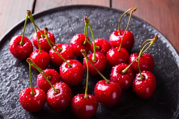 Cherries on a black plate. Sweet cherries on a wooden board. Red berries in water drops. Top view. Copy space