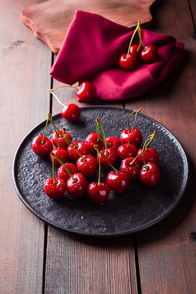Cherries on a black plate. Sweet cherries on a wooden board. Red berries in water drops. Top view. Copy space