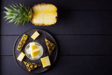 Koyu renkli bir arka planda ananas. Siyah bir tabakta dilimlenmiş ananas. Buz ve ananas dilimleri ile içilir. Aşılanmış su. Kopyalama alanı