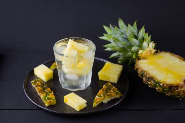 Koyu renkli bir arka planda ananas. Siyah bir tabakta dilimlenmiş ananas. Buz ve ananas dilimleri ile içilir. Aşılanmış su. Kopyalama alanı