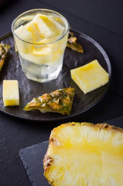 Koyu renkli bir arka planda ananas. Siyah bir tabakta dilimlenmiş ananas. Buz ve ananas dilimleri ile içilir. Aşılanmış su. Kopyalama alanı