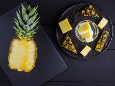 Koyu renkli bir arka planda ananas. Siyah bir tabakta dilimlenmiş ananas. Buz ve ananas dilimleri ile içilir. Aşılanmış su. Kopyalama alanı