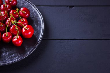 Siyah tabakta kırmızı kirazlar. Karanlık bir arka plan üzerinde su damlatatlı kiraz. Vegan için kırmızı meyveler. Üst te. Kopyalama alanı