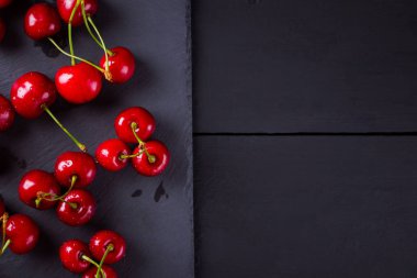 Kayrak tahtasında kiraz. Karanlık bir arka planda tatlı kirazlar. Siyah tahtalarda su damlalarında kırmızı meyveler. Sağlıklı yiyecekler. Üst te. Kopyalama alanı