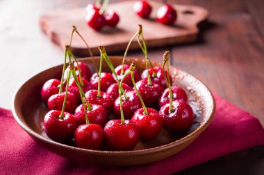 Kil tabakta kiraz. Tahta tahtada tatlı kirazlar. Kırmızı peçetede su damlalarında kırmızı meyveler. Rustik tarz. Kopyalama alanı