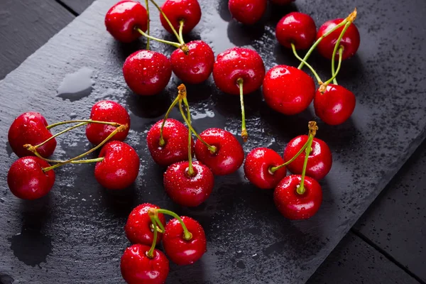 Cherries on a slate board. Sweet cherries on a dark background. Red berries in drops of water on black boards. Healthy food. Top view. Copy space