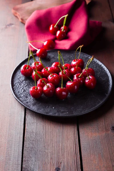 Cherries on a black plate. Sweet cherries on a wooden board. Red berries in water drops. Top view. Copy space