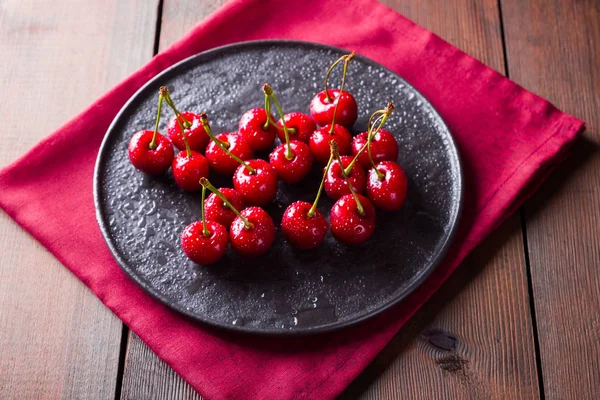 Cherries on a black plate. Sweet cherries on a wooden board. Red berries in water drops. Top view. Copy space