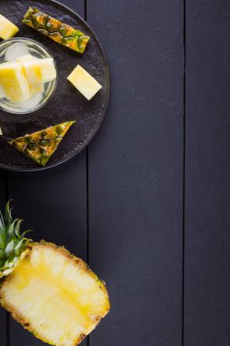 Koyu renkli bir arka planda ananas. Siyah bir tabakta dilimlenmiş ananas. Buz ve ananas dilimleri ile içilir. Aşılanmış su. Kopyalama alanı