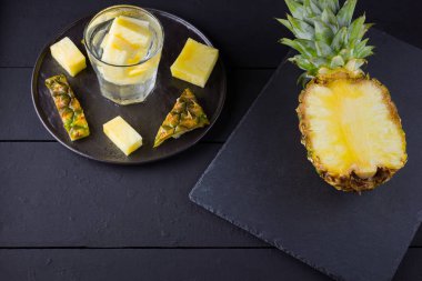 Koyu renkli bir arka planda ananas. Siyah bir tabakta dilimlenmiş ananas. Buz ve ananas dilimleri ile içilir. Aşılanmış su. Kopyalama alanı