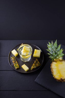 Koyu renkli bir arka planda ananas. Siyah bir tabakta dilimlenmiş ananas. Buz ve ananas dilimleri ile içilir. Aşılanmış su. Kopyalama alanı