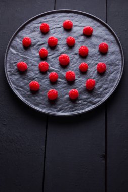 Koyu bir arka plan üzerinde ahududu. Siyah tabakta kırmızı ahududu. Tahta tahtalarda kırmızı meyveler. Üst te. Kopyalama alanı