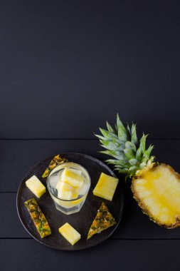 Koyu renkli bir arka planda ananas. Siyah bir tabakta dilimlenmiş ananas. Buz ve ananas dilimleri ile içilir. Aşılanmış su. Kopyalama alanı