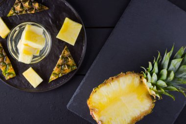 Koyu renkli bir arka planda ananas. Siyah bir tabakta dilimlenmiş ananas. Buz ve ananas dilimleri ile içilir. Aşılanmış su. Kopyalama alanı