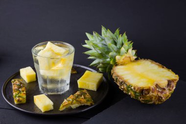 Koyu renkli bir arka planda ananas. Siyah bir tabakta dilimlenmiş ananas. Buz ve ananas dilimleri ile içilir. Aşılanmış su. Kopyalama alanı