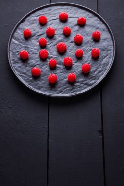 Koyu bir arka plan üzerinde ahududu. Siyah tabakta kırmızı ahududu. Tahta tahtalarda kırmızı meyveler. Üst te. Kopyalama alanı