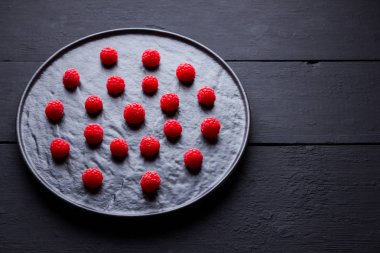 Koyu bir arka plan üzerinde ahududu. Siyah tabakta kırmızı ahududu. Tahta tahtalarda kırmızı meyveler. Üst te. Kopyalama alanı