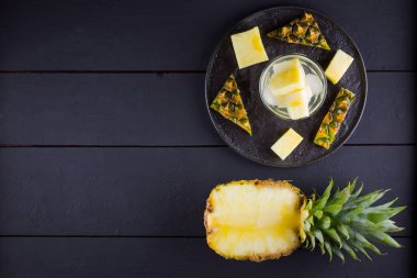Koyu renkli bir arka planda ananas. Siyah bir tabakta dilimlenmiş ananas. Buz ve ananas dilimleri ile içilir. Aşılanmış su. Kopyalama alanı