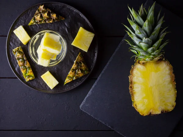 Pineapple on a dark background. Sliced pineapple on a black plate. Drink with ice and pineapple slices. Infused water. Copy space