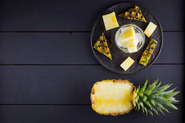 Pineapple on a dark background. Sliced pineapple on a black plate. Drink with ice and pineapple slices. Infused water. Copy space