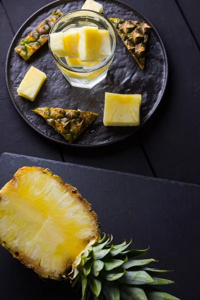 Koyu renkli bir arka planda ananas. Siyah bir tabakta dilimlenmiş ananas. Buz ve ananas dilimleri ile içilir. Aşılanmış su. Kopyalama alanı