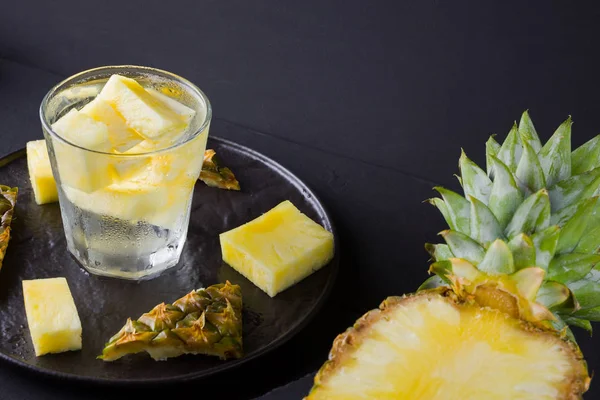 Pineapple on a dark background. Sliced pineapple on a black plate. Drink with ice and pineapple slices. Infused water. Copy space