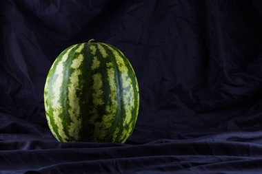 Siyah kumaş üzerine karpuz. Koyu zeminde bütün karpuz. Vegan için sağlıklı bir besin. Kopyalama alanı