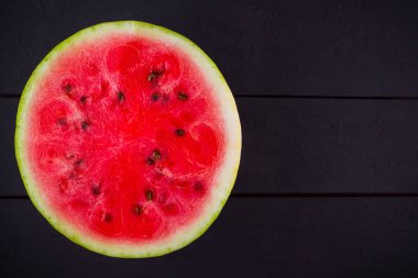 Karpuzun yarısı koyu zeminde. Tahta tahtalarda dilimlenmiş karpuz. Vegan için sağlıklı bir besin. Üstte görüntü