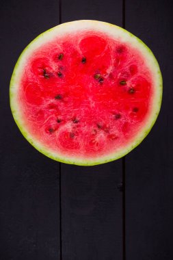 Karpuzun yarısı koyu zeminde. Tahta tahtalarda dilimlenmiş karpuz. Vegan için sağlıklı bir besin. Üstte görüntü