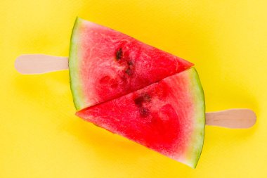 Karpuz dilimi sarı bir arka plan üzerinde açılır. Tahta çubuklar üzerinde tatlı karpuz. Yaz konsepti