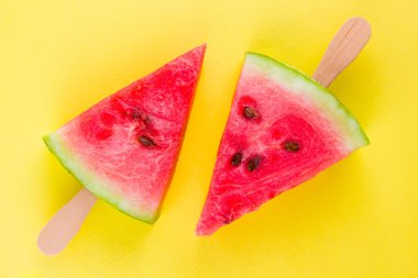Karpuz dilimi sarı bir arka plan üzerinde açılır. Tahta çubuklar üzerinde tatlı karpuz. Yaz konsepti