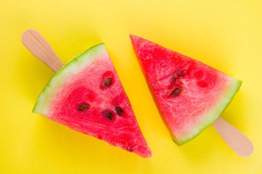 Karpuz dilimi sarı bir arka plan üzerinde açılır. Tahta çubuklar üzerinde tatlı karpuz. Yaz konsepti